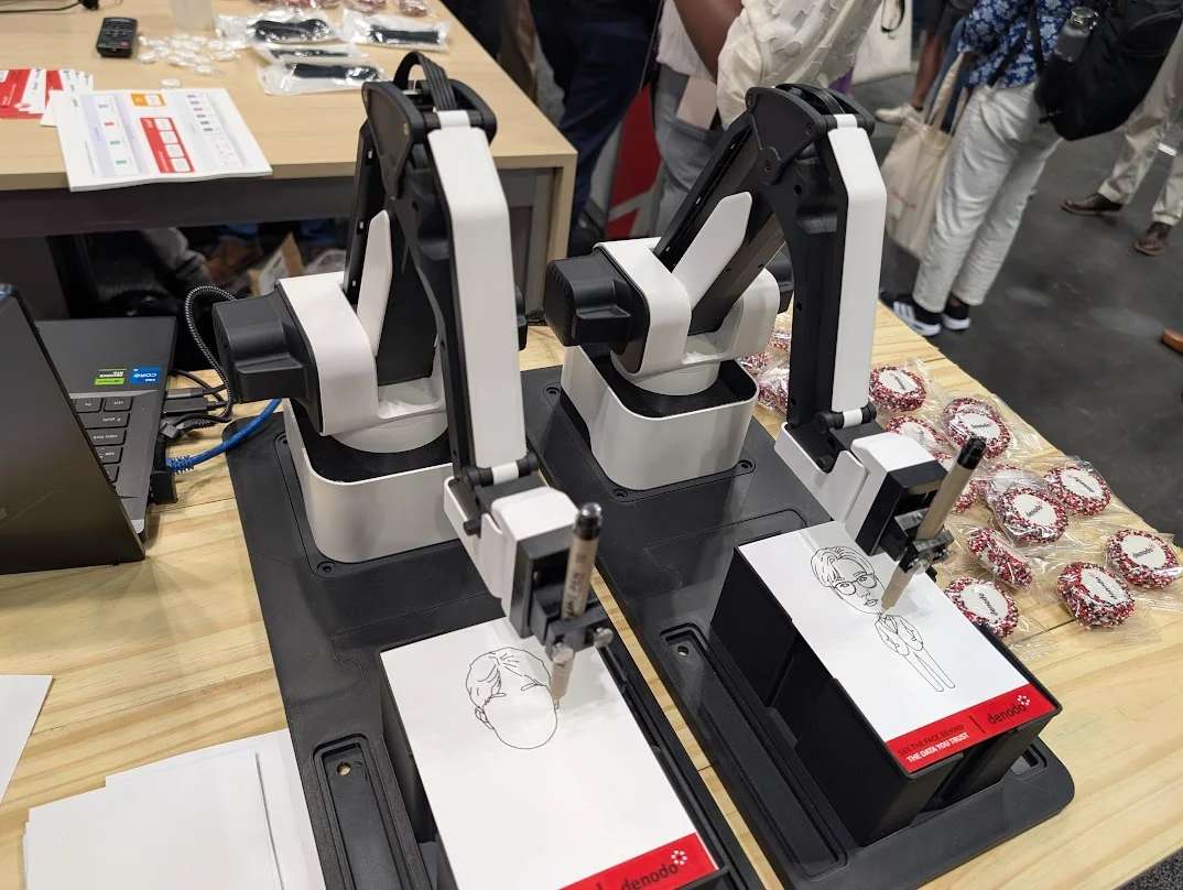 Sketch bot rental NYC — twin robot sketch artists drawing live AI portraits at a corporate trade show